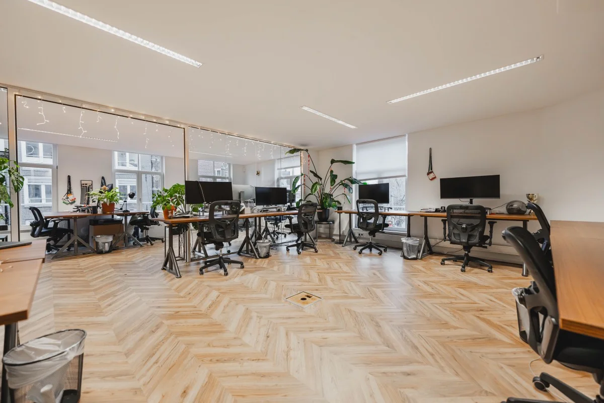 Modern kantoorinterieur aan de Korte Reguliersdwarsstraat met bureaus, bureaustoelen, computerschermen en kamerplanten.